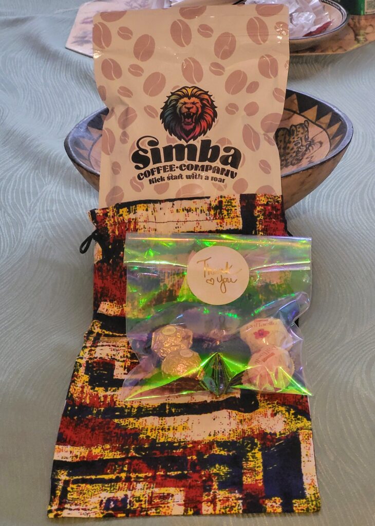 A colorful bag of Simba Coffee Company coffee sits next to a treat bag labeled "Thank You," containing chocolates and candies, on a patterned tablecloth.