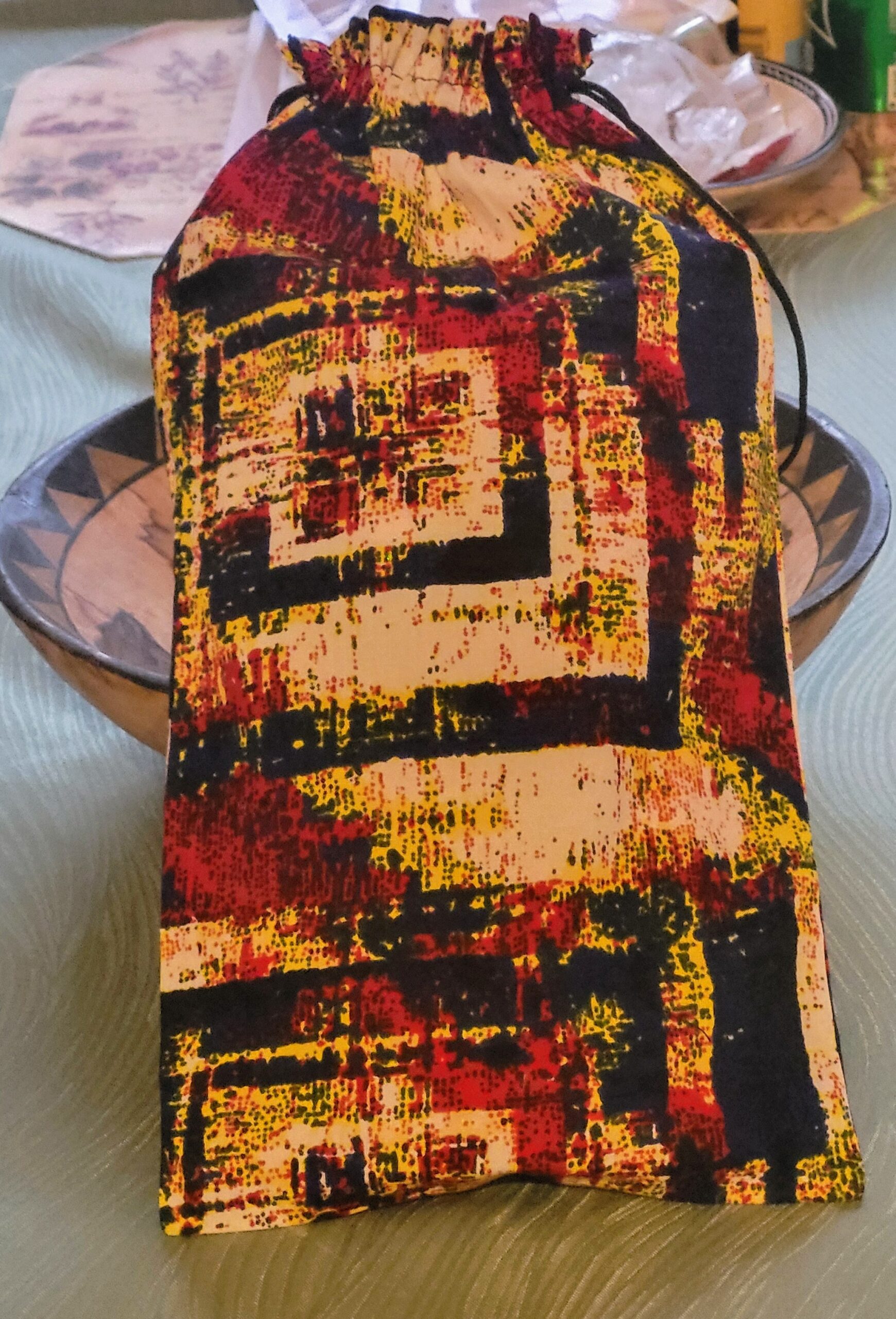 Colorful drawstring bag with a geometric pattern in red, yellow, and black, placed on a textured green table. Ideal for organizing small items.